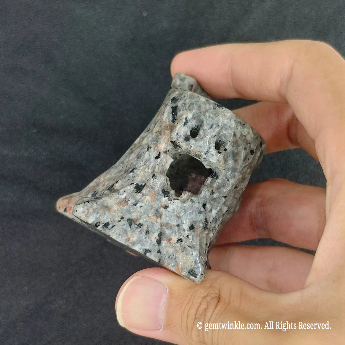 Side angle of flame stone tree spirit figurine resting in hand displaying carved bark surface