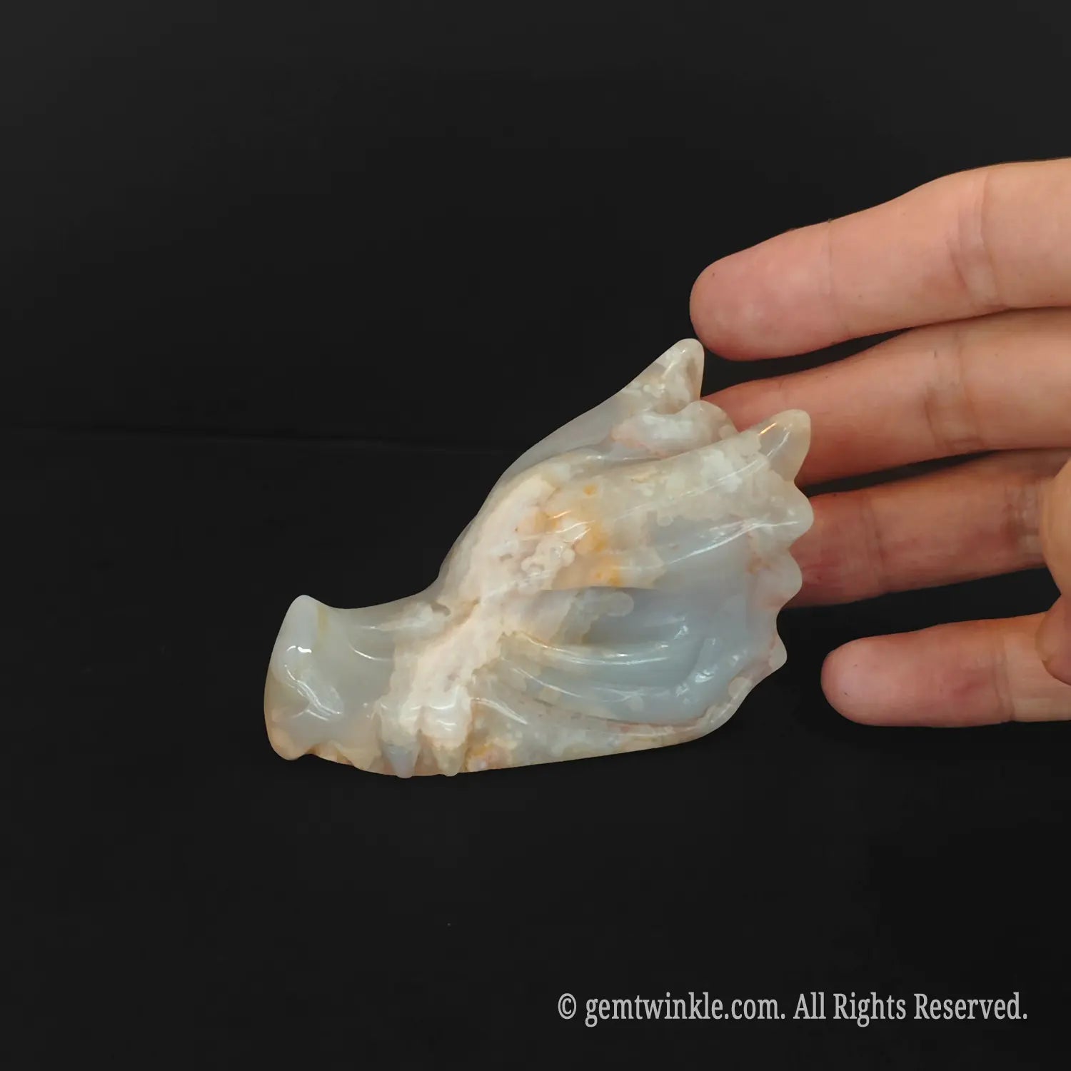 A close up of a hand checking the polished back and horns of a cherry blossom agate dragon skull figurine for retail store inventory