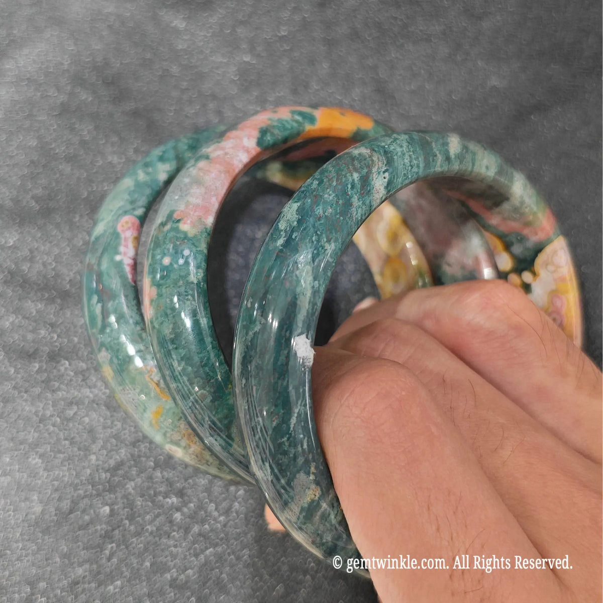 Fingertips holding flower skin ocean jasper bangles highlighting smooth polish and natural circular orb inclusions