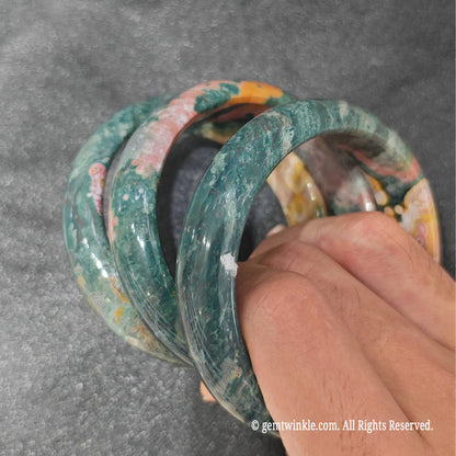 Fingertips holding flower skin ocean jasper bangles highlighting smooth polish and natural circular orb inclusions