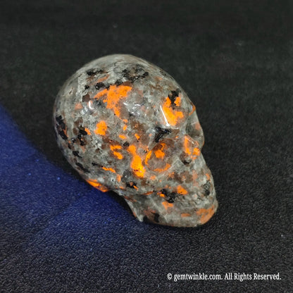 Carved yooperlite crystal skull glowing with fiery orange sodalite ember spots under 365nm UV blacklight