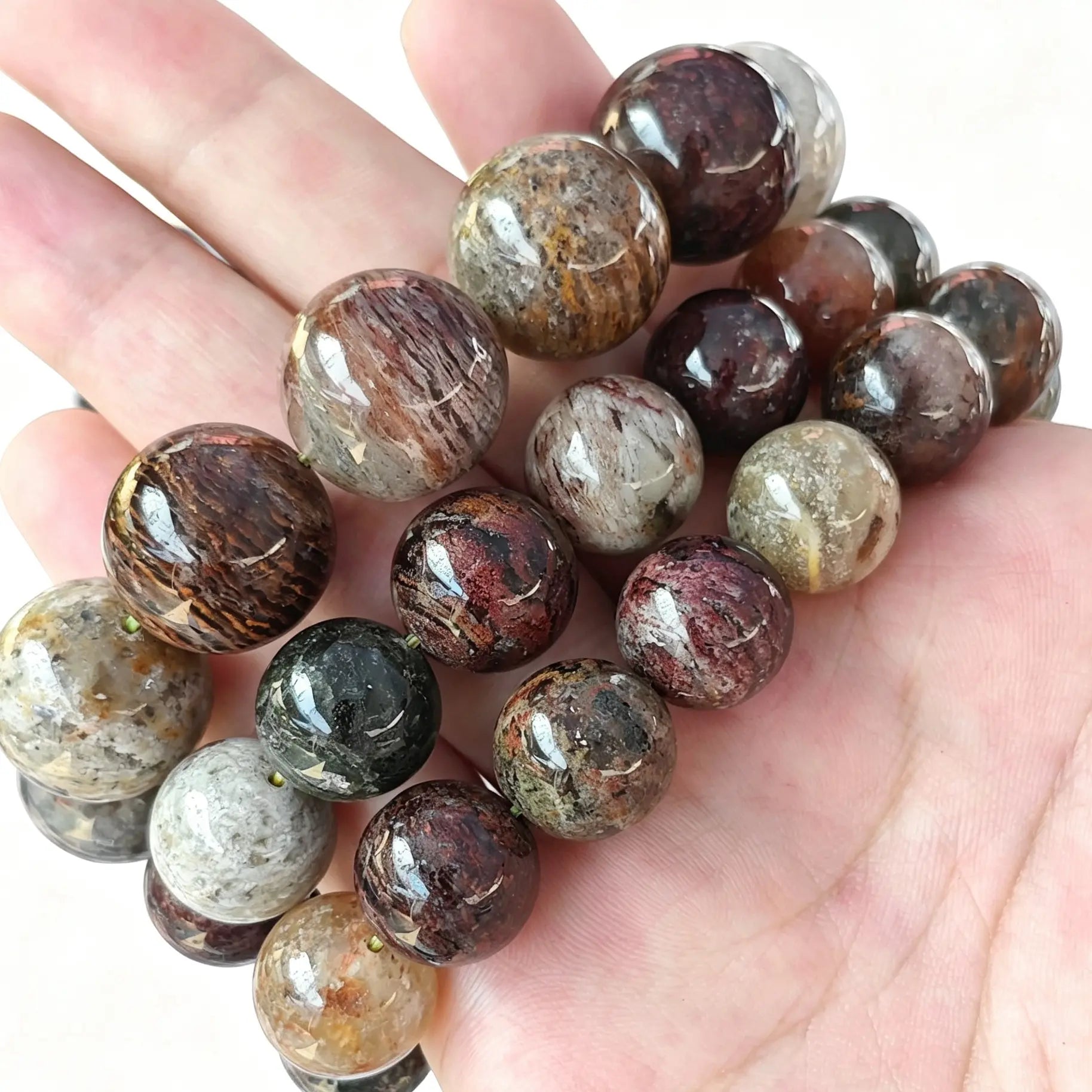 Main view of stacked multi-color Four Seasons phantom quartz round bead bracelets resting on palm showing rich mineral inclusions