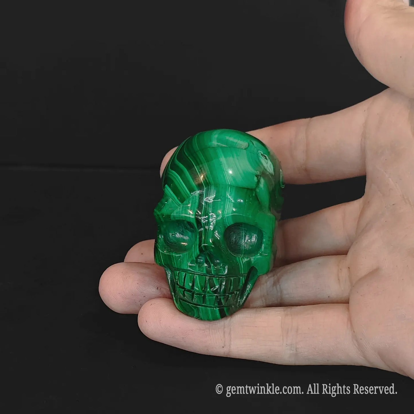 Front view of a natural malachite gemstone skull resting on a palm