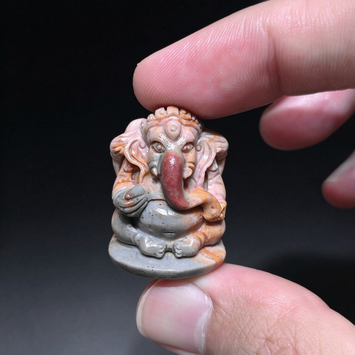Frontal view of a carved stone Ganesha figurine in terracotta red and slate gray held between fingertips