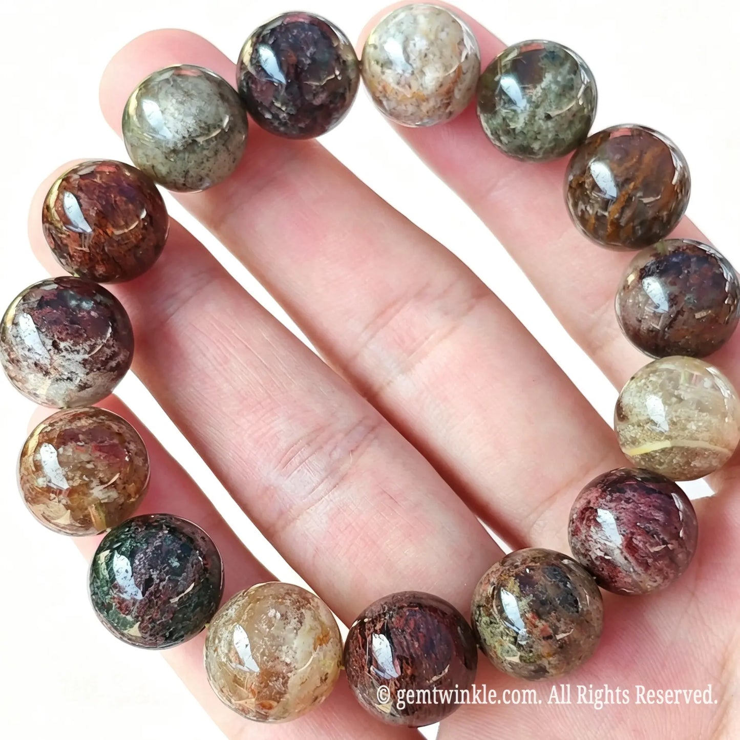 Single strand Four Seasons phantom quartz bead bracelet looped over open hand displaying red, green, and yellow inclusions