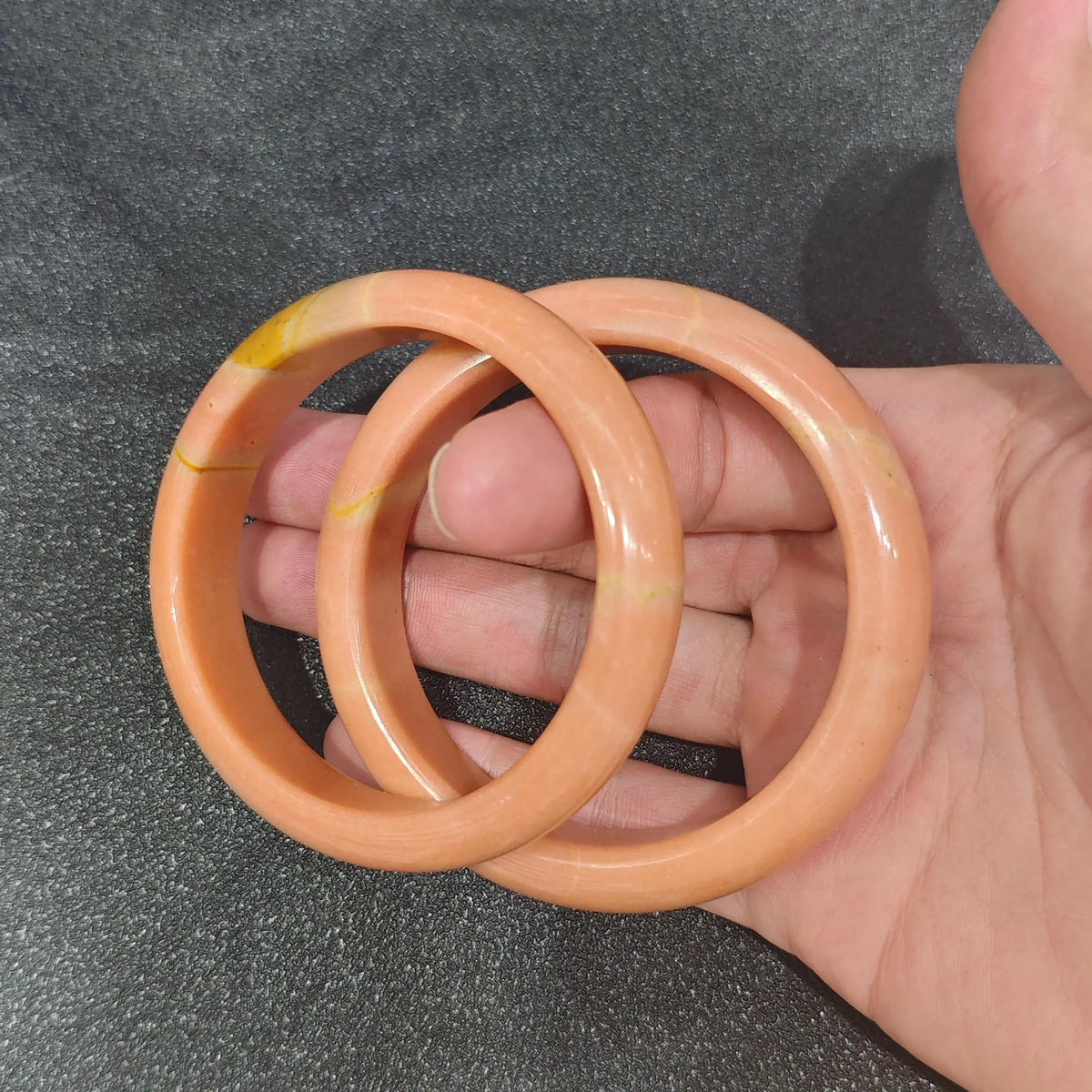Gem's Twinkle Natural Apricot Quartz solid gemstone bangle bracelet held on hand in warm cinnamon orange tones