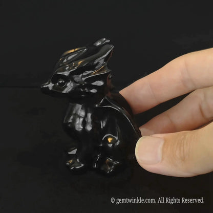 Side profile of a polished black obsidian baby dragon figurine showing glossy wing details and sleek dark contours