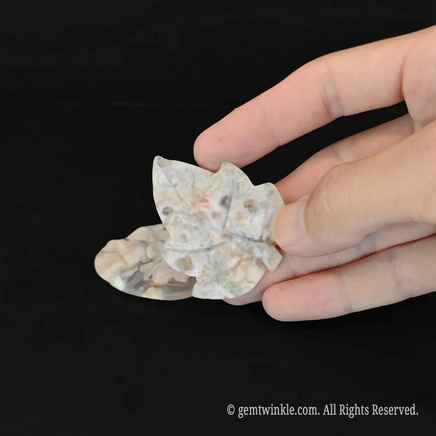 Handheld view of a cherry blossom agate leaf crystal carving showing detailed carved recessed veins and fine polish