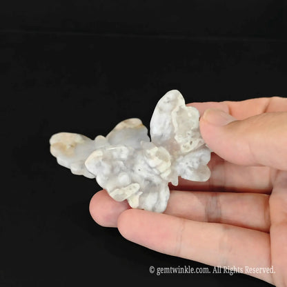 Handheld view of a cherry blossom agate butterfly crystal carving showing polished wing edges and natural mineral textures