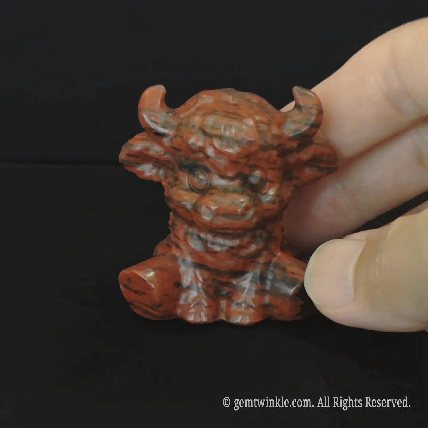 Front profile of the polished mahogany obsidian cow carving highlighting rich brick red splotches and smooth contours