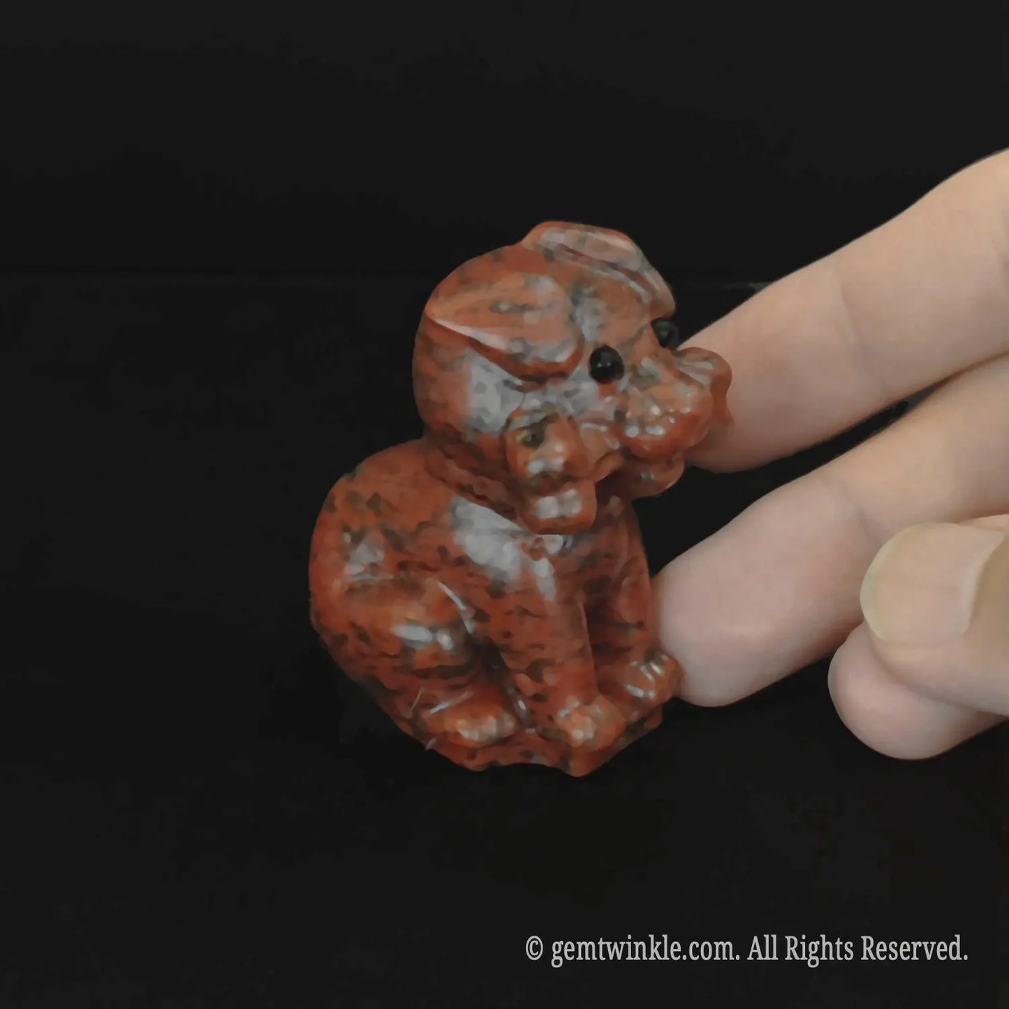 Side profile view of the 5cm mahogany obsidian puppy figurine showcasing rich brick red and black patterns