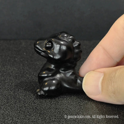 Hand-sculpted 4cm mini black obsidian baby dinosaur figurine held in hand showing direct wholesale source quality