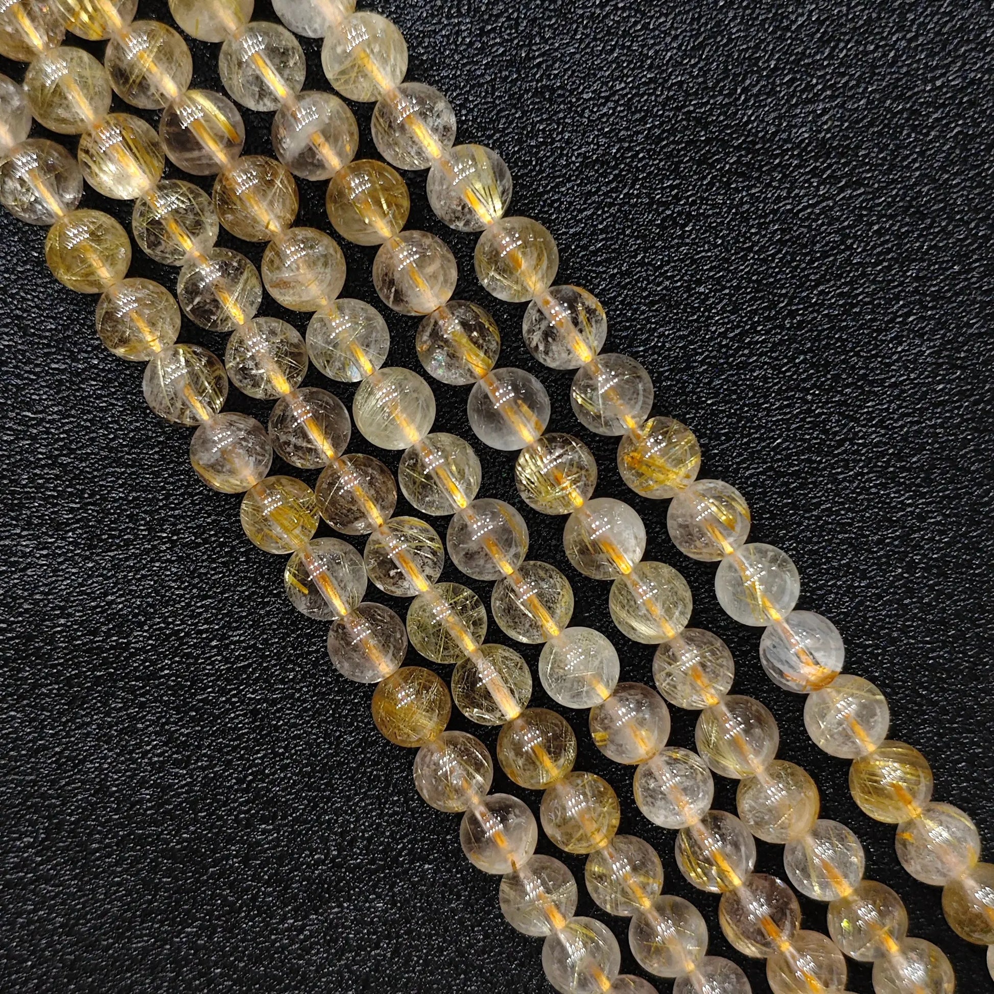 Close up look of natural gold rutilated quartz strands showing dense golden needle inclusions inside 8mm round beads on a dark background