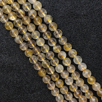 Close up look of natural gold rutilated quartz strands showing dense golden needle inclusions inside 8mm round beads on a dark background