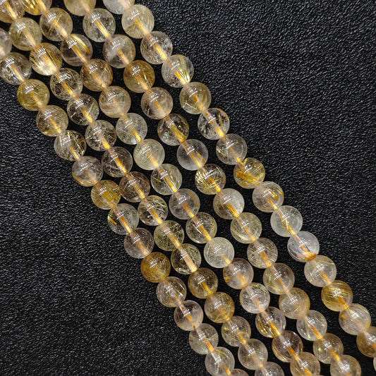 Close up look of natural gold rutilated quartz strands showing dense golden needle inclusions inside 8mm round beads on a dark background