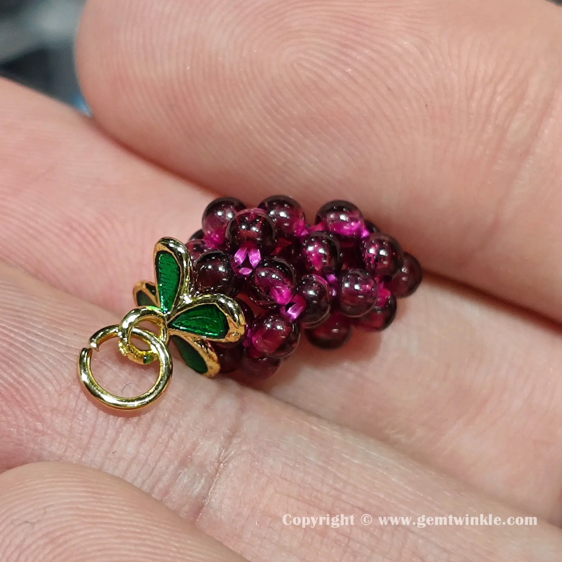 Handheld side view of genuine garnet grape fruit charm showcasing its deep wine red glossy finish on hand