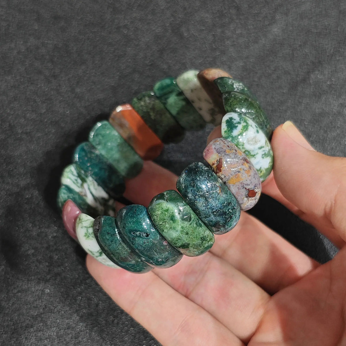 Genuine ocean agate nodule bead stretch bracelet held on hand showing 24x11mm deep forest green and pinkish white mineral patterns