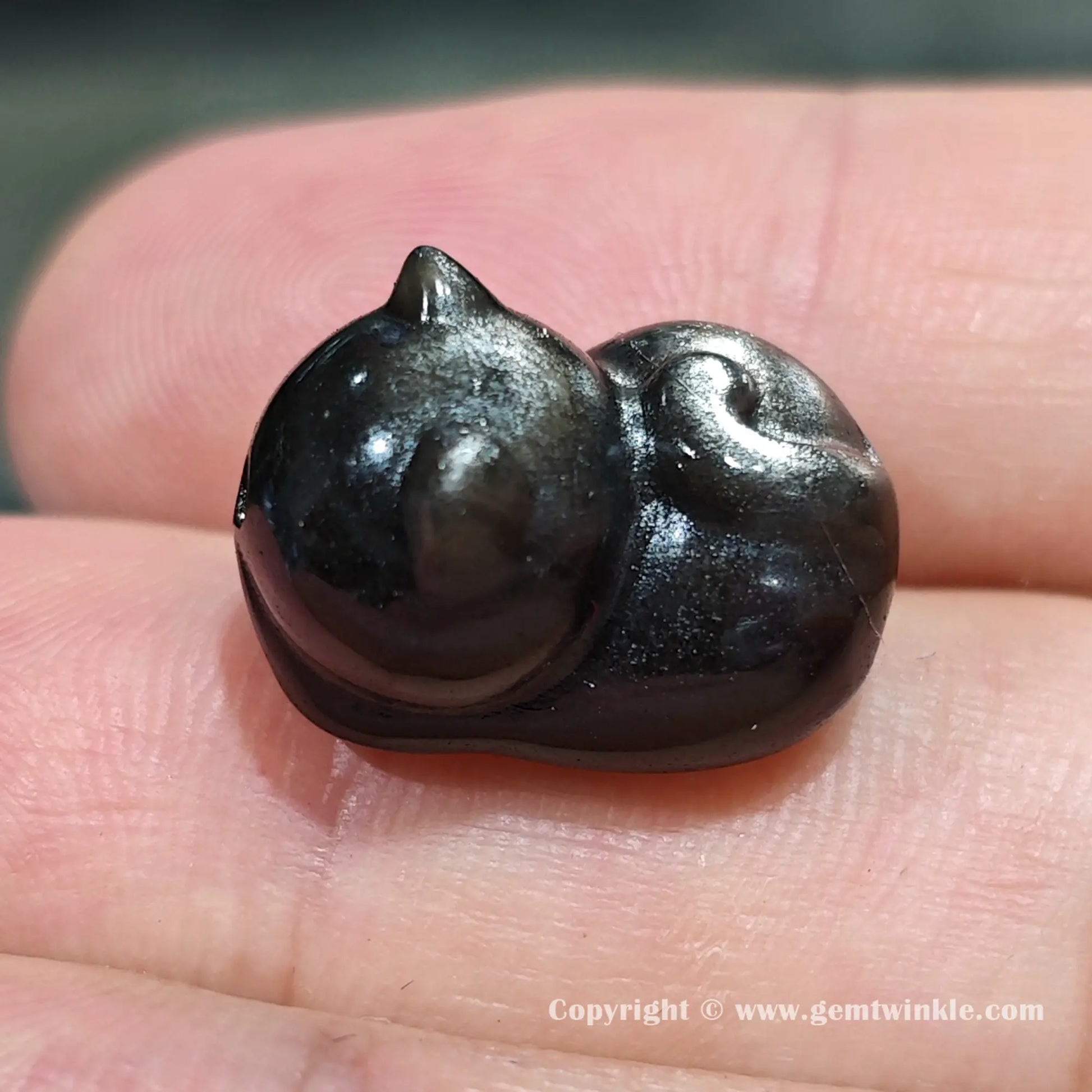 Back view of genuine silver sheen obsidian sleeping cat charm bead showing size proportions on fingers
