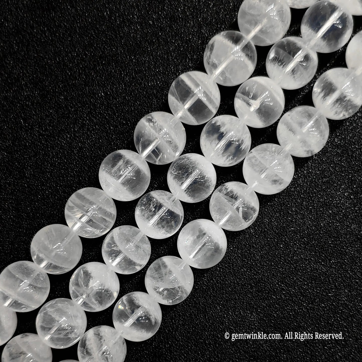 three strands of polished white phantom crystal beads laid diagonally on a black background