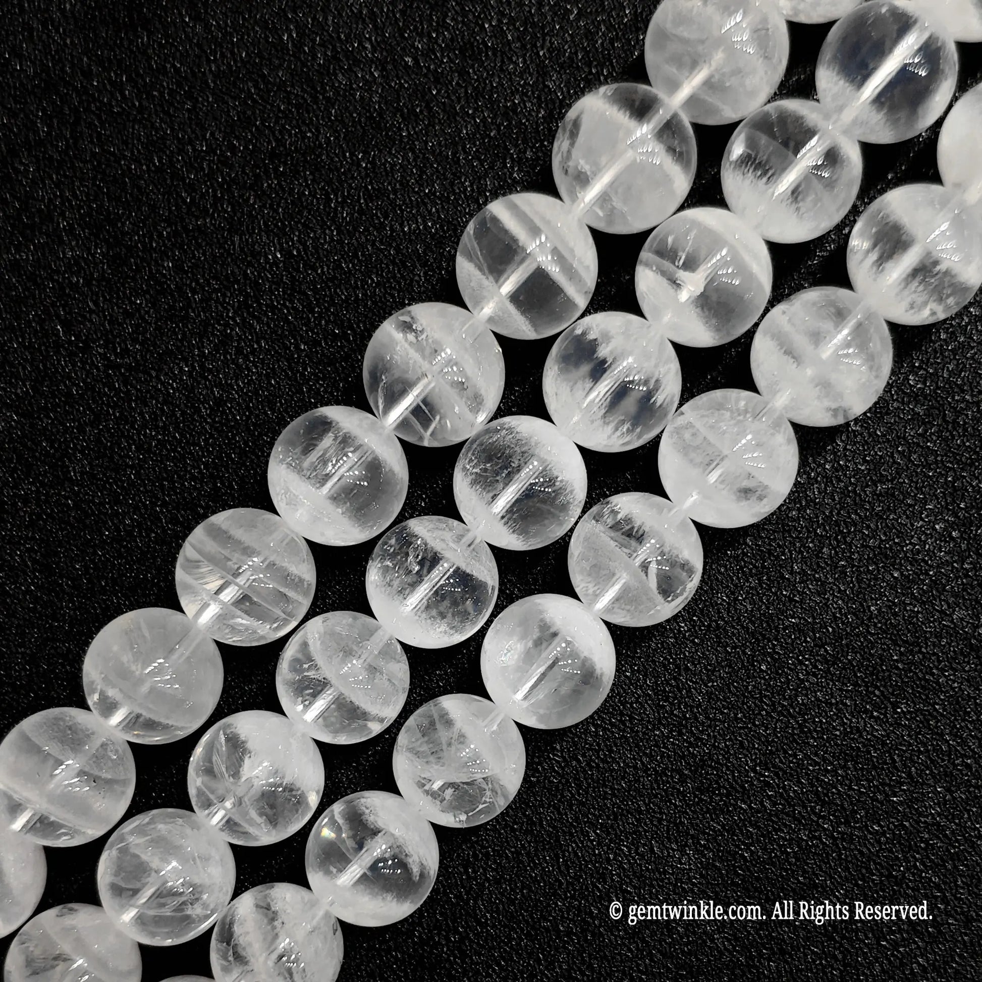 three strands of polished white phantom crystal beads laid diagonally on a black background