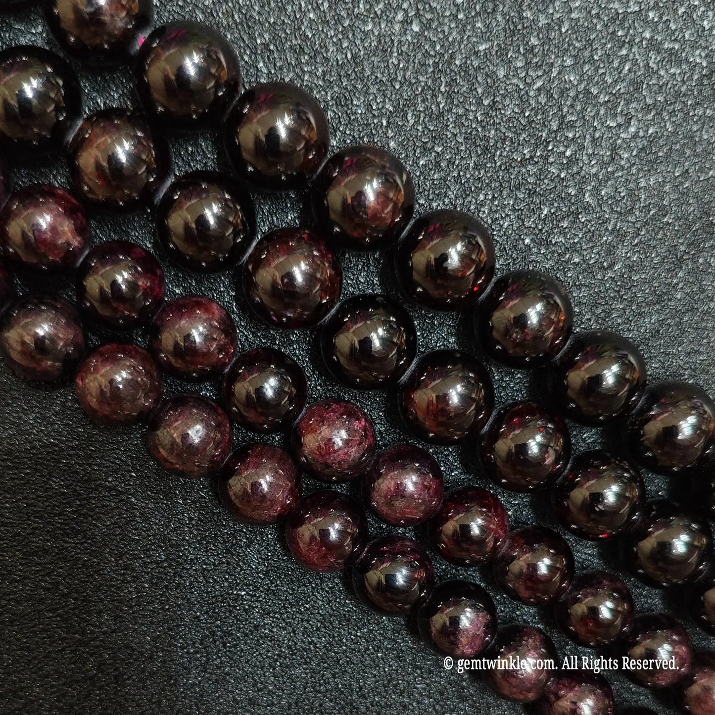 three loose strands of grade c red garnet beads on black background showing natural textures