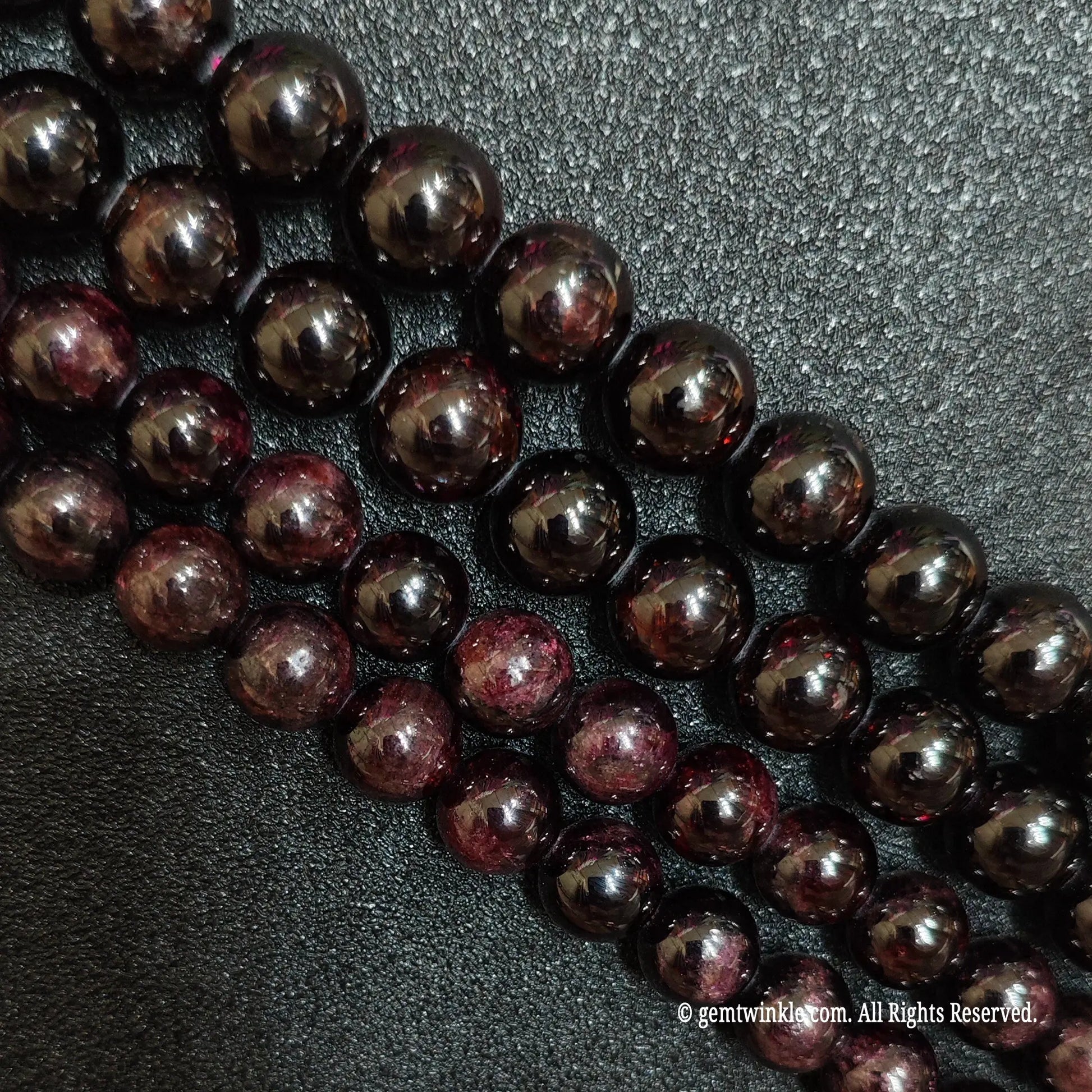 three loose strands of grade c red garnet beads on black background showing natural textures