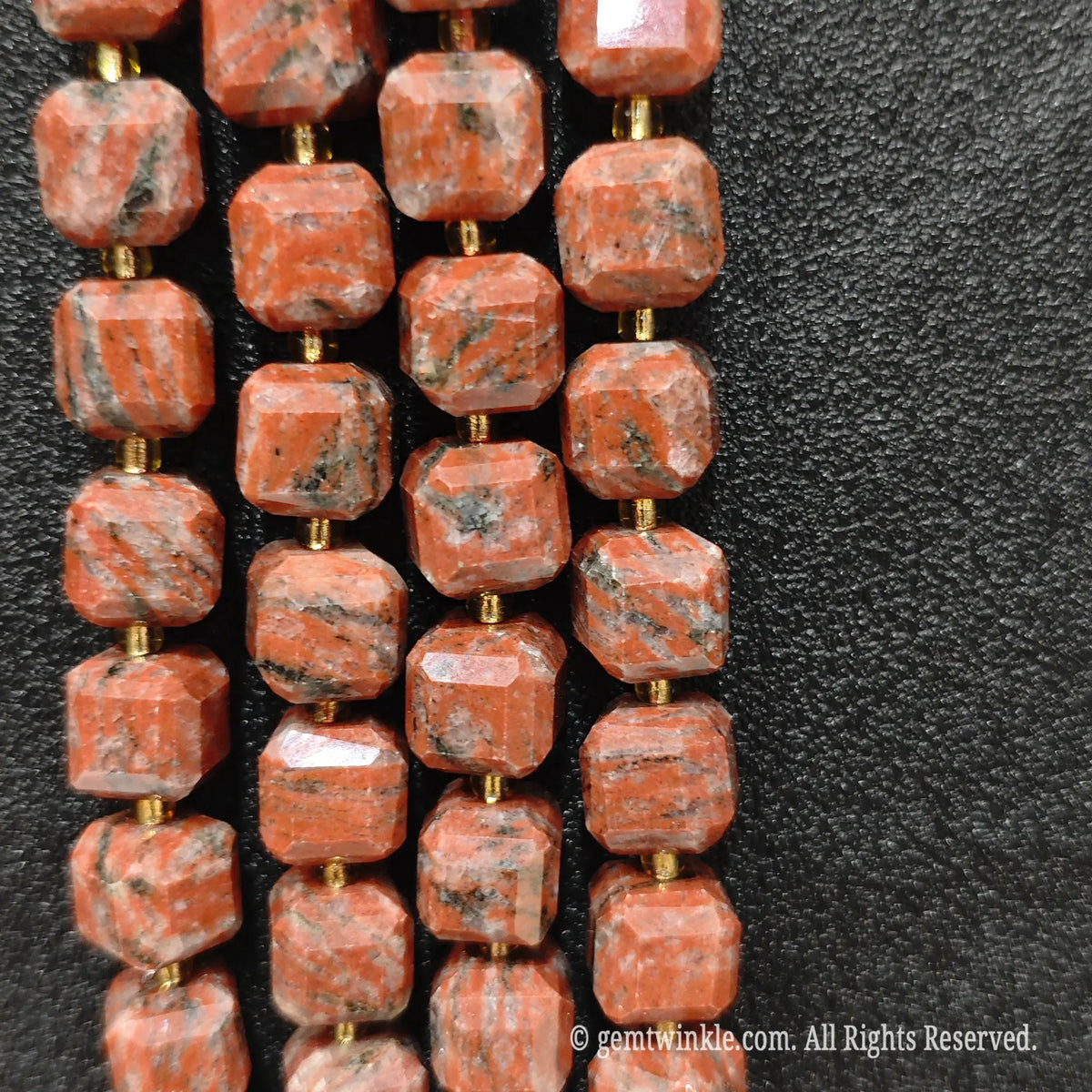 Angled presentation of red sesame jasper strands highlighting their polished finish and drill holes