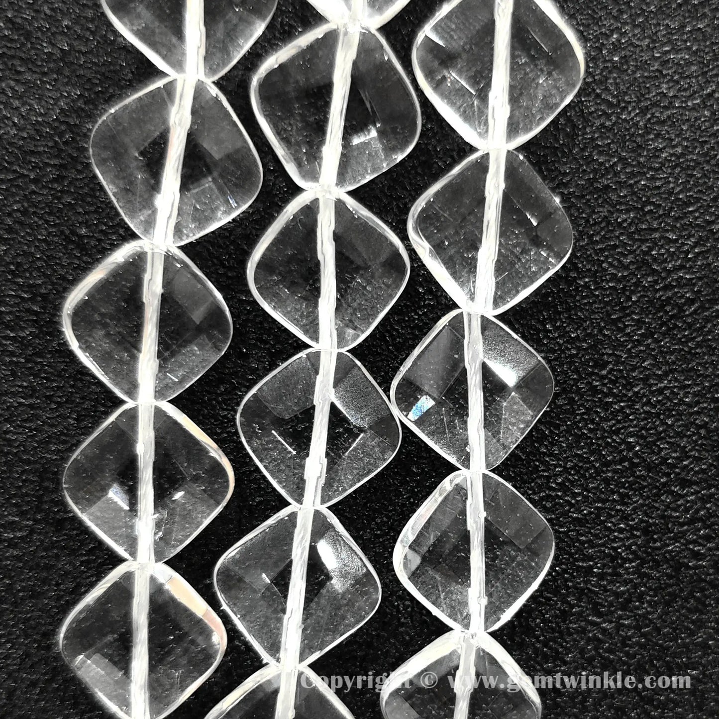 Vertical layout of geometric flat diamond carved clear quartz beads on dark surface