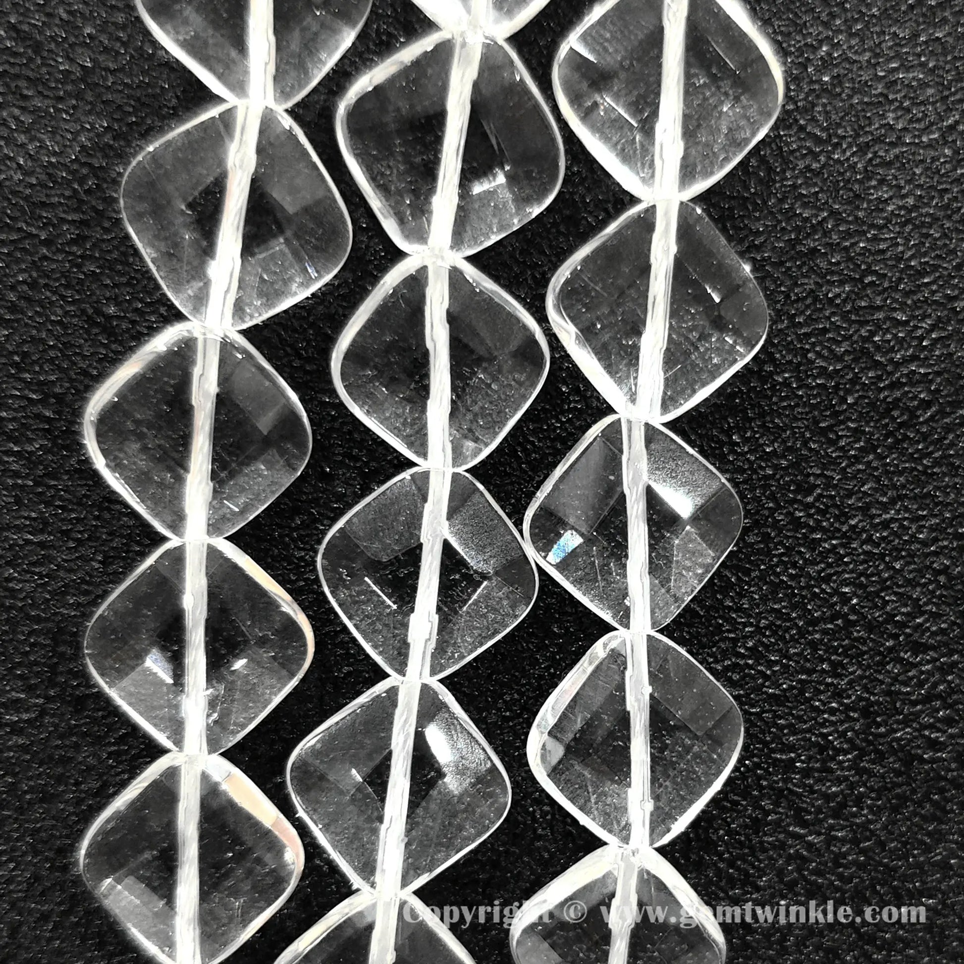 Vertical layout of geometric flat diamond carved clear quartz beads on dark surface