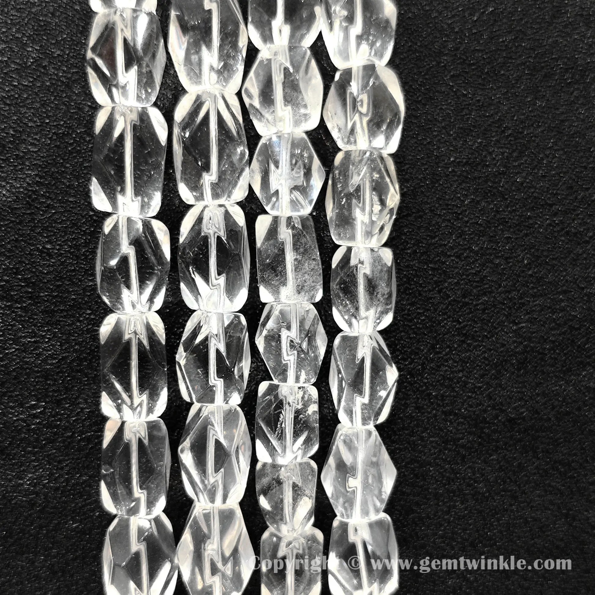 Vertical layout of geometric faceted clear quartz barrel beads on dark surface