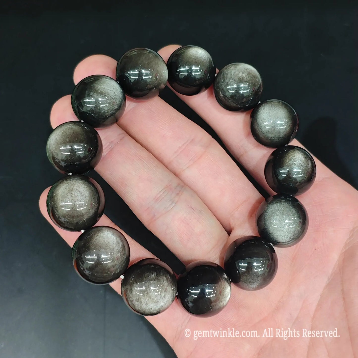 Glossy black silver cat's eye obsidian stretch bracelet top view showing uniform round bead alignment and mirror shine