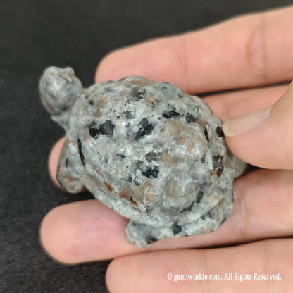Close up view of glowing yooperlite sea turtle statue held in palm displaying smooth matte hand polish