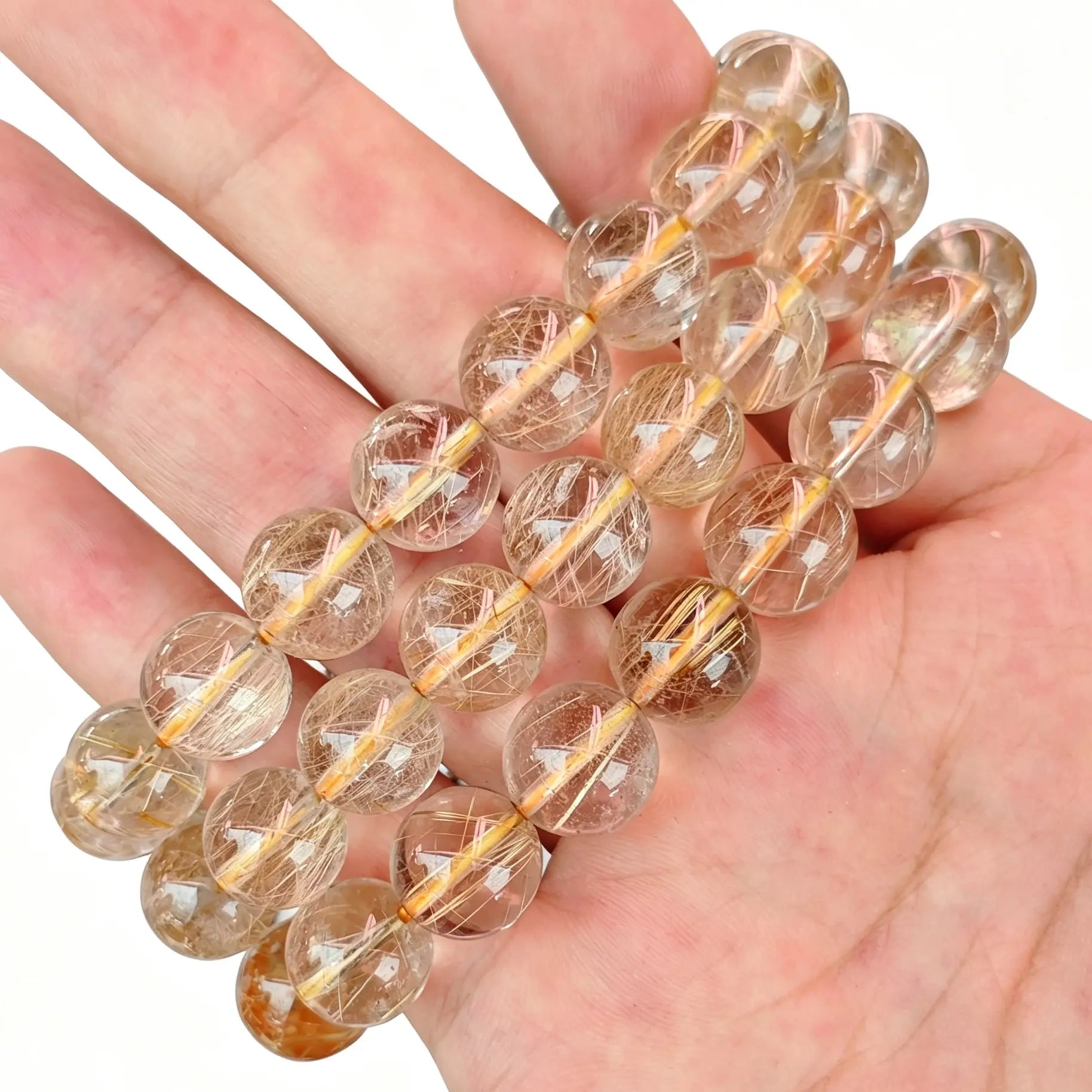 Single-strand gold rutilated quartz round bead bracelet held on fingers showing fine rutile needles