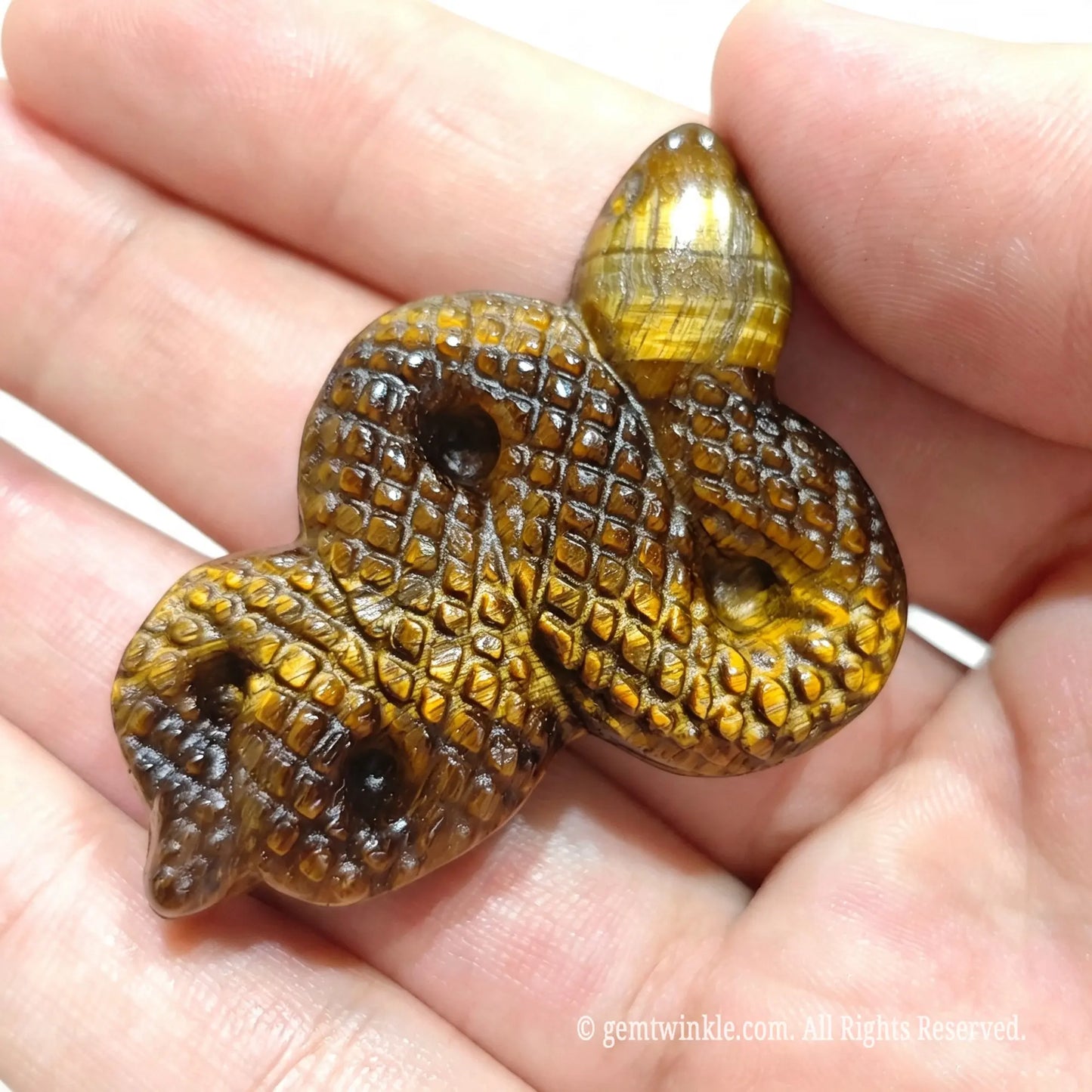 Close up view of gold tiger eye serpent statue in hand highlighting snake head and golden optical sheen