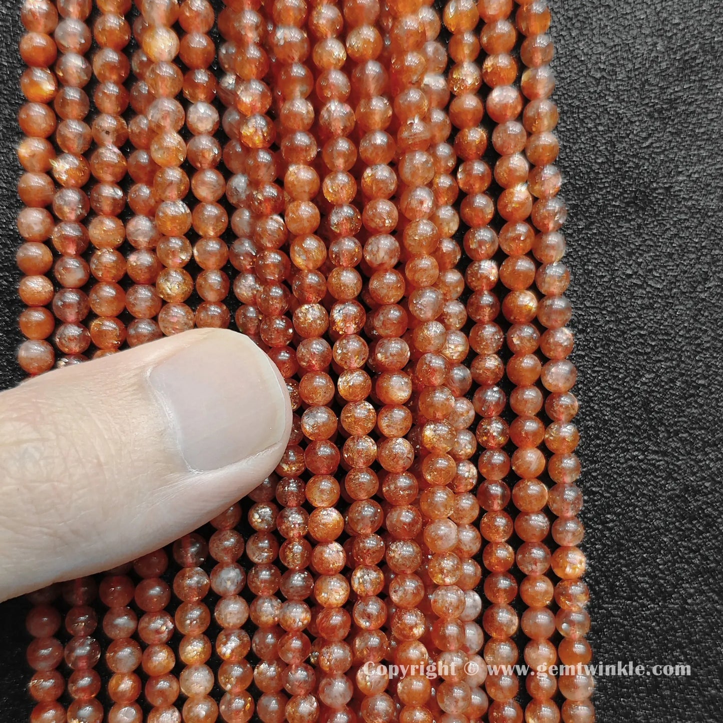 Close up view of natural golden sunstone 4mm micro round beads inspected on fingers for quality preview