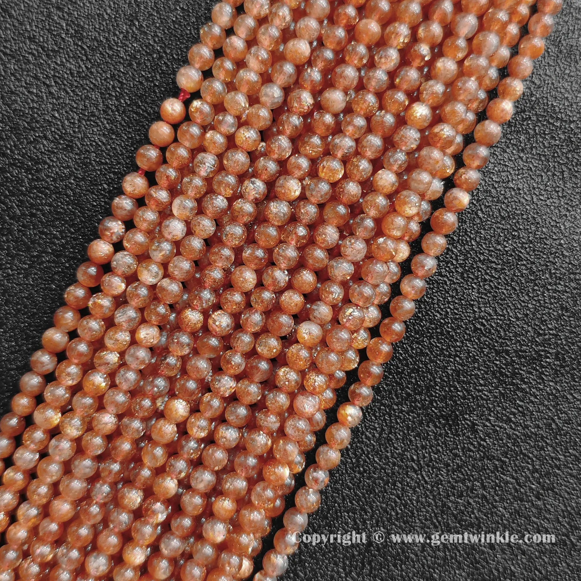 Angled view of natural orange golden sunstone 4mm micro bead strands arranged parallel on dark background