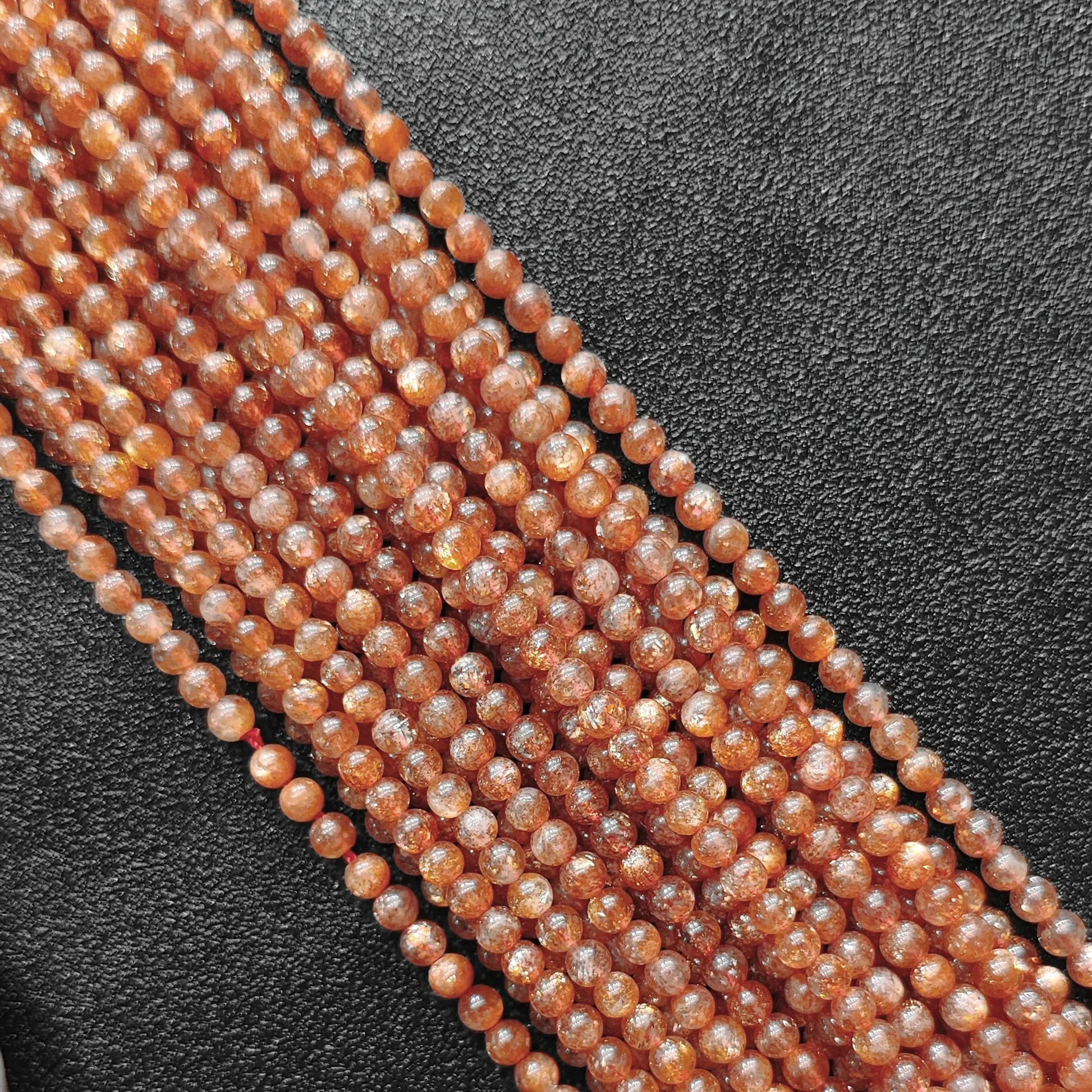 Macro closeup of natural golden sunstone B plus grade 4mm smooth round beads showing intense copper sparkle