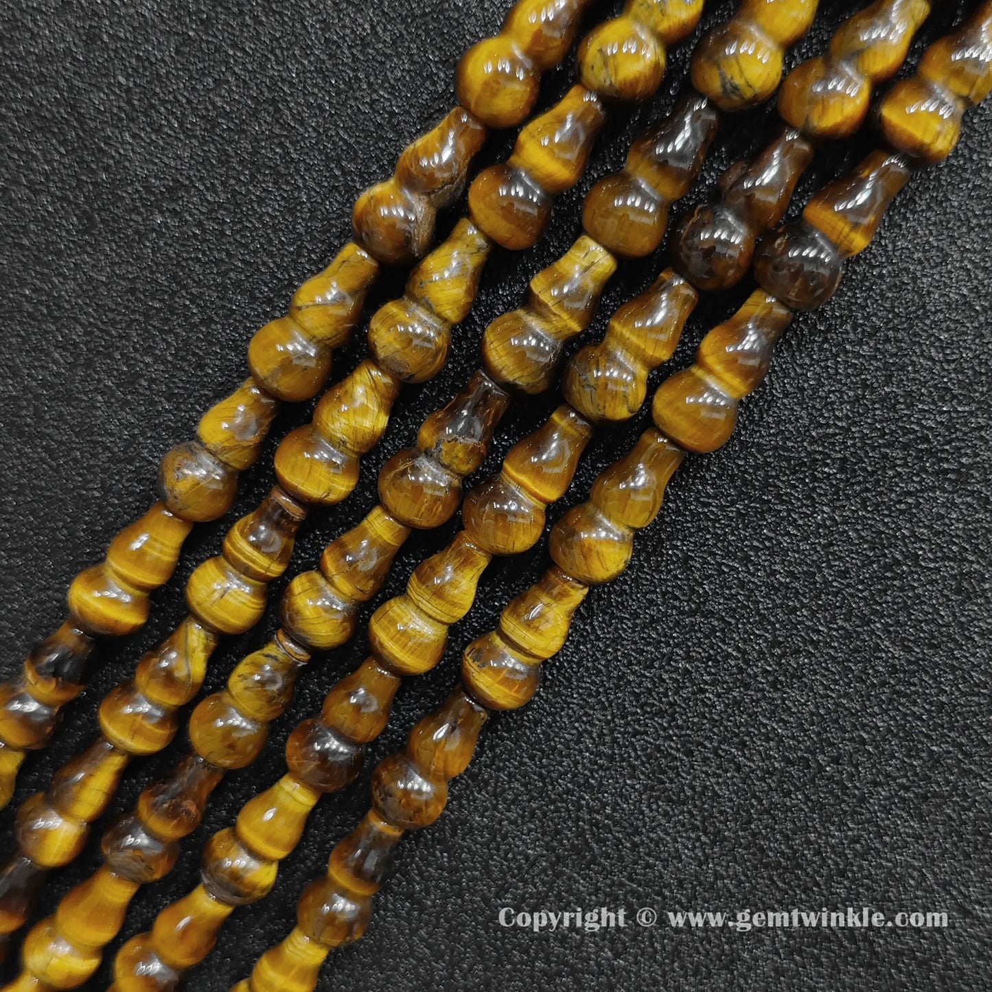 Angled view of natural golden yellow tiger eye calabash cut gemstone strands