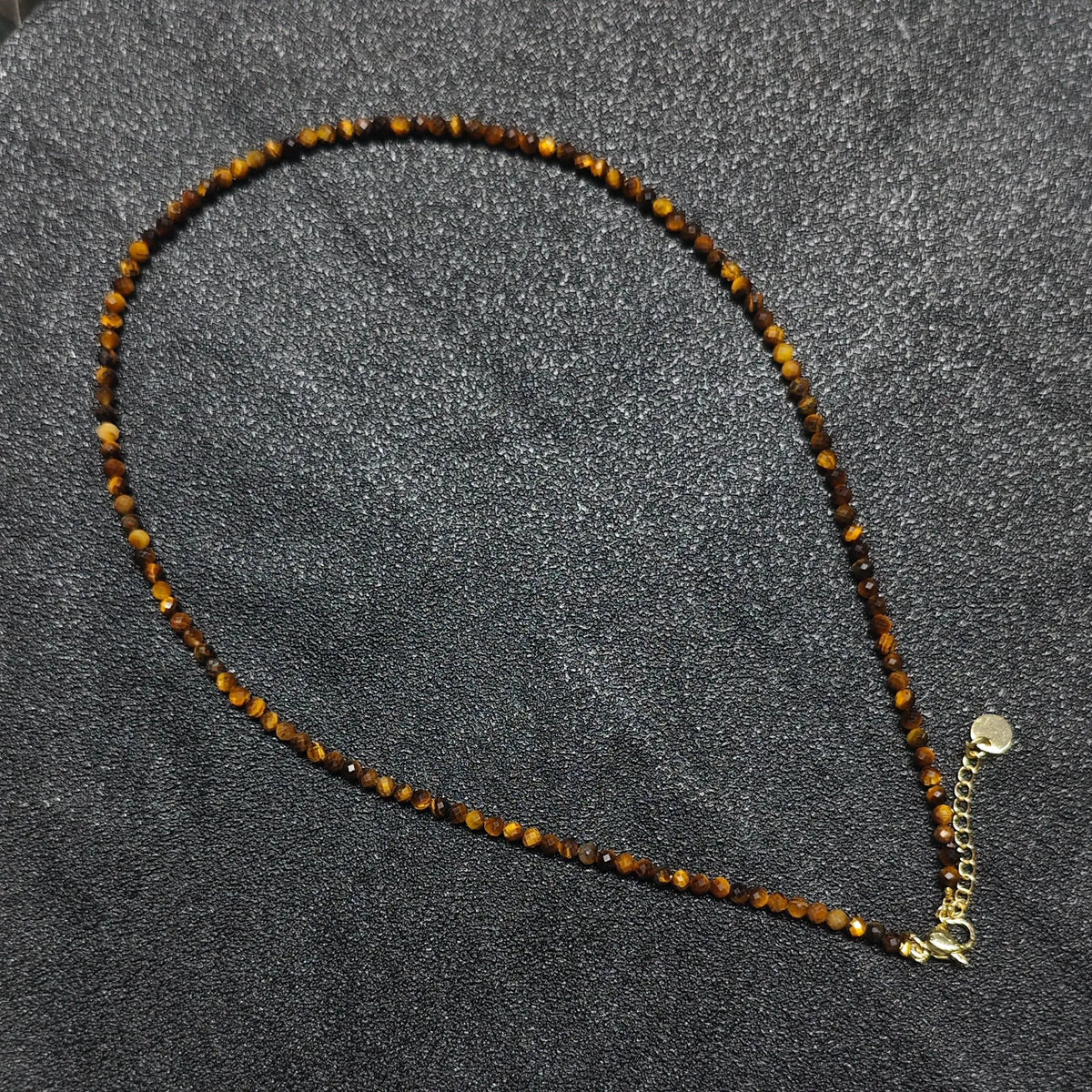 Hand holding 3mm micro faceted Golden Tiger Eye necklace strand showing silky golden brown cat eye chatoyancy