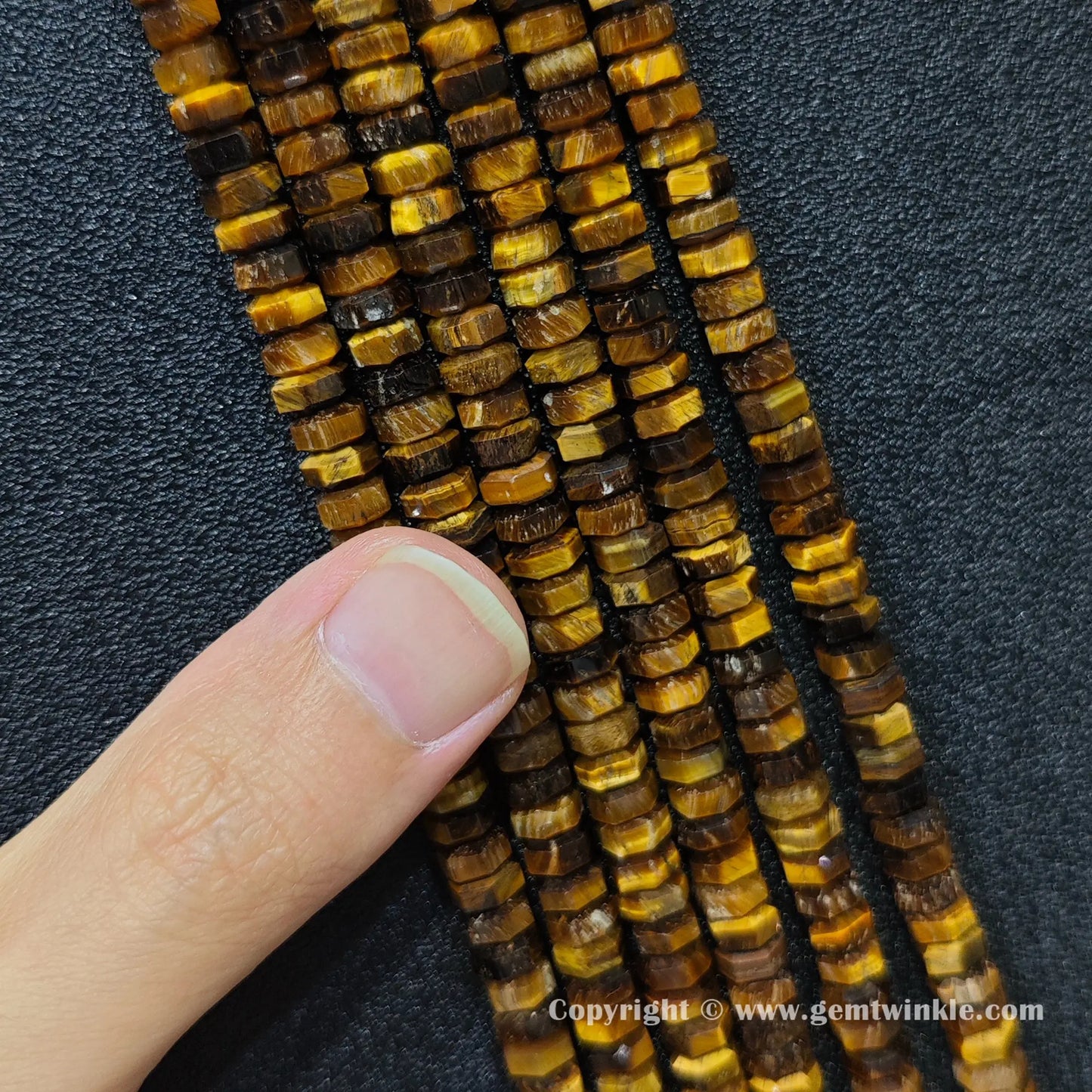 Close up view of 6x3mm golden tiger eye faceted disc rondelle beads inspected on fingers for quality preview