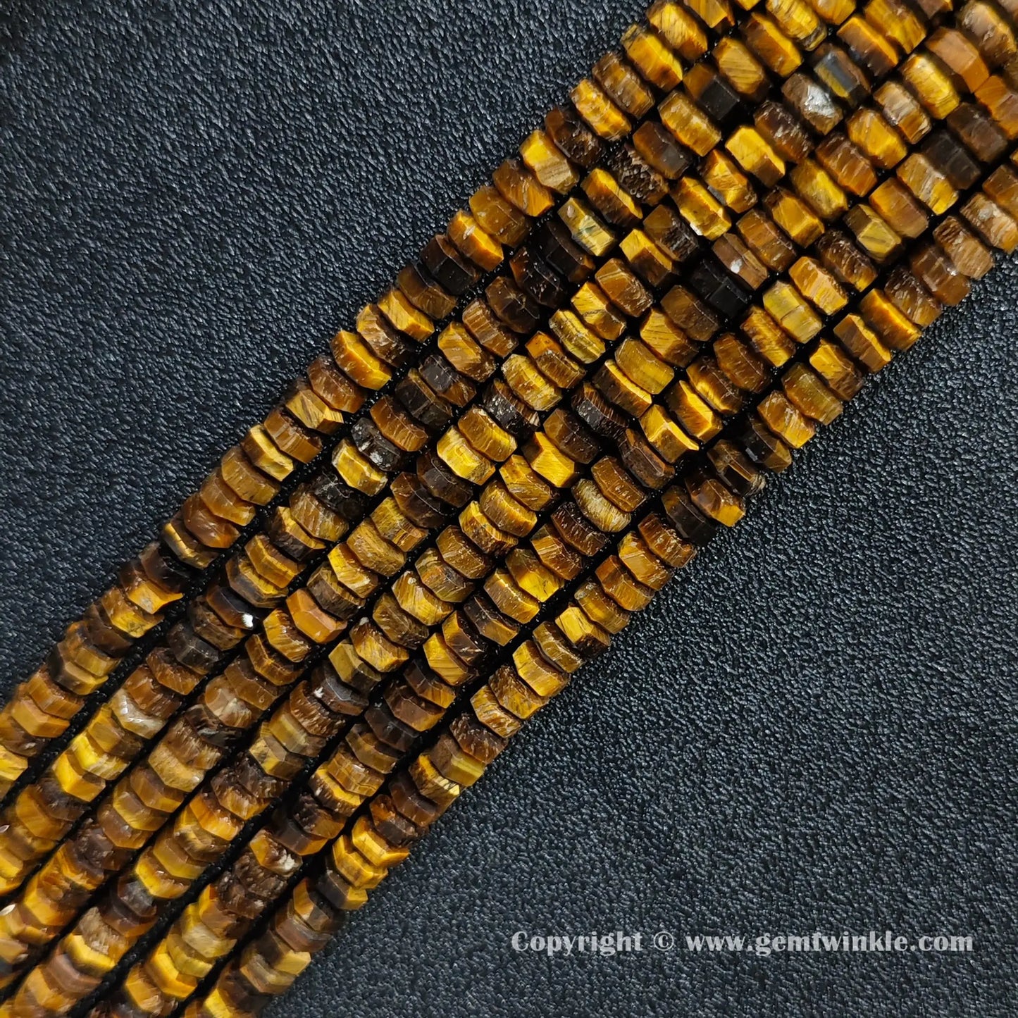 Angled view of natural golden tiger eye faceted disc gemstone strands arranged parallel on dark background