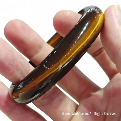 Angled hand view of a solid golden tiger eye crystal bangle showing warm honey brown color and smooth inner contour
