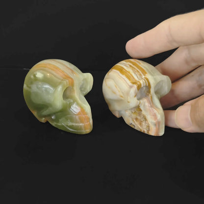 A hand holding a polished ocean jasper skull carving to demonstrate its 6cm size and flat base