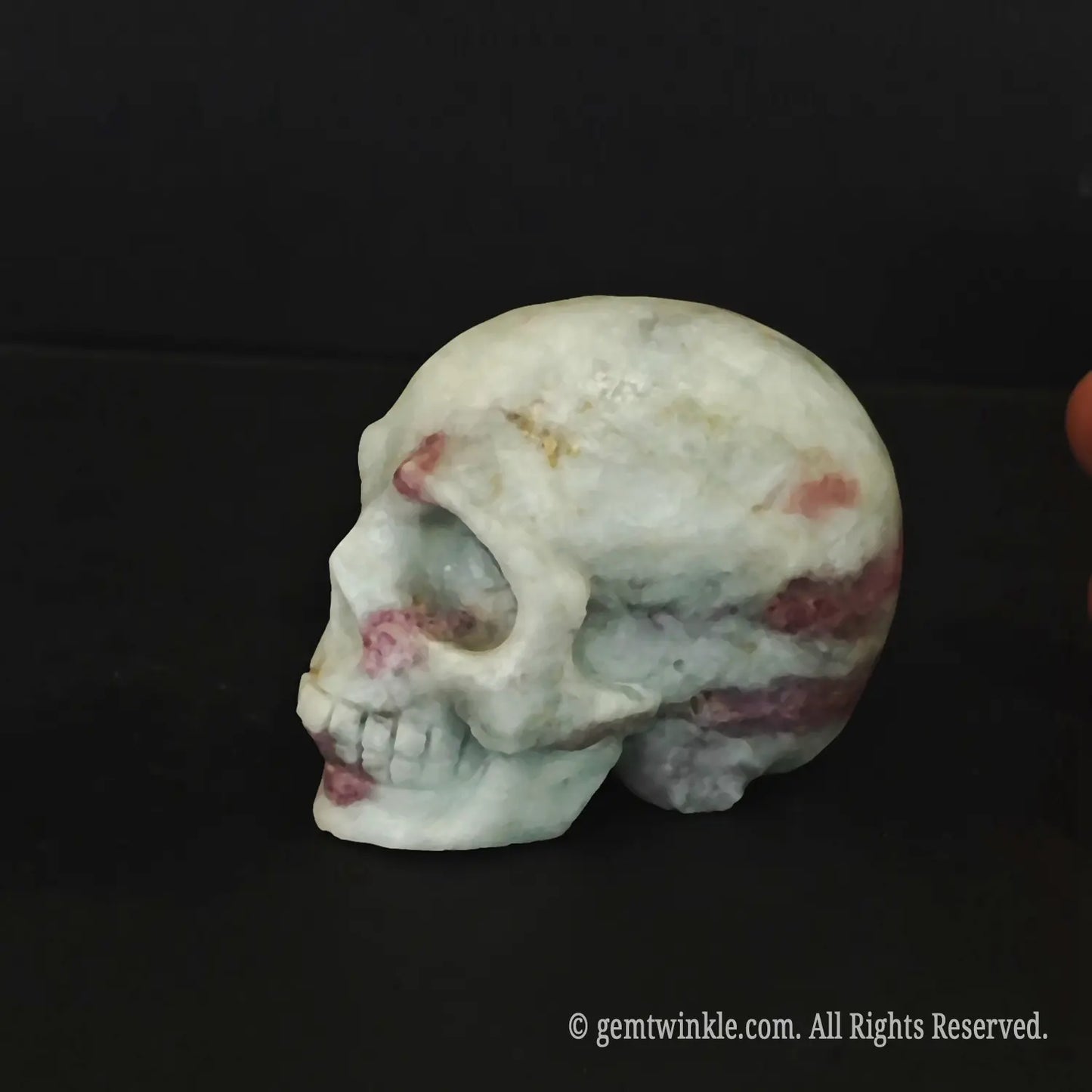 A hand holding a polished pink tourmaline quartz human skull figurine showing its flat base and 6cm size