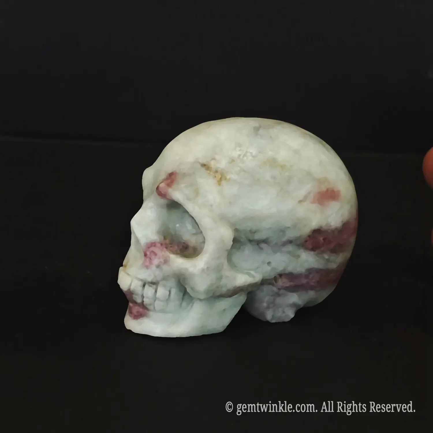A hand holding a polished pink tourmaline quartz human skull figurine showing its flat base and 6cm size