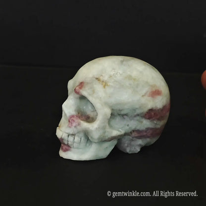 A hand holding a polished pink tourmaline quartz human skull figurine showing its flat base and 6cm size