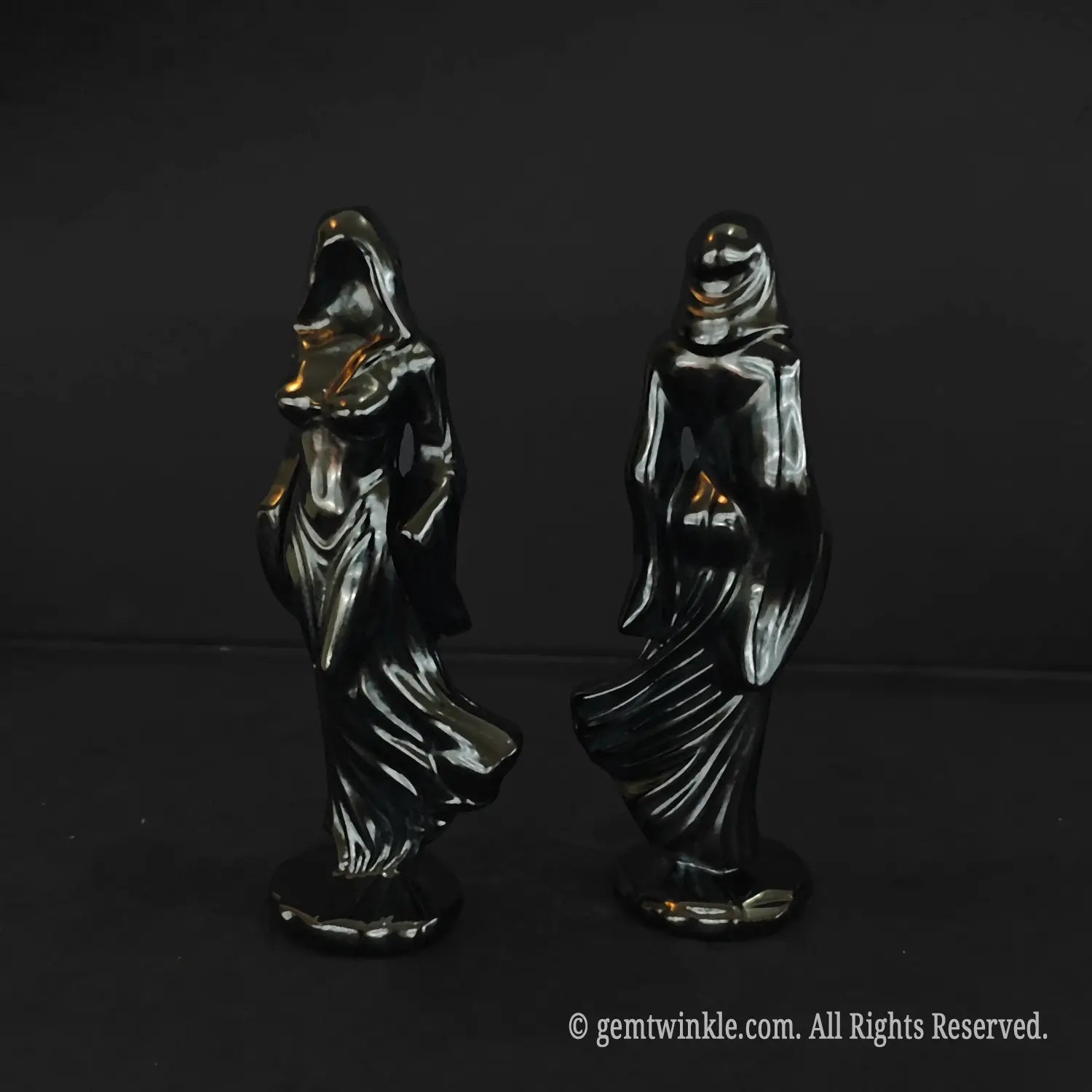 Side profiles of two black obsidian cloaked figures highlighting the dynamic wind swept flowing dress lines