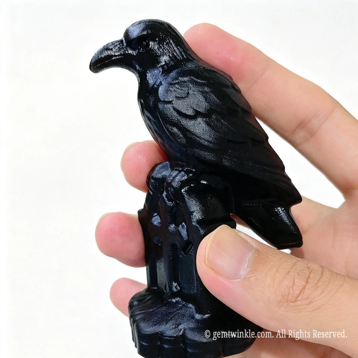 Side profile of black obsidian crow carving on tombstone base held in hand against white background