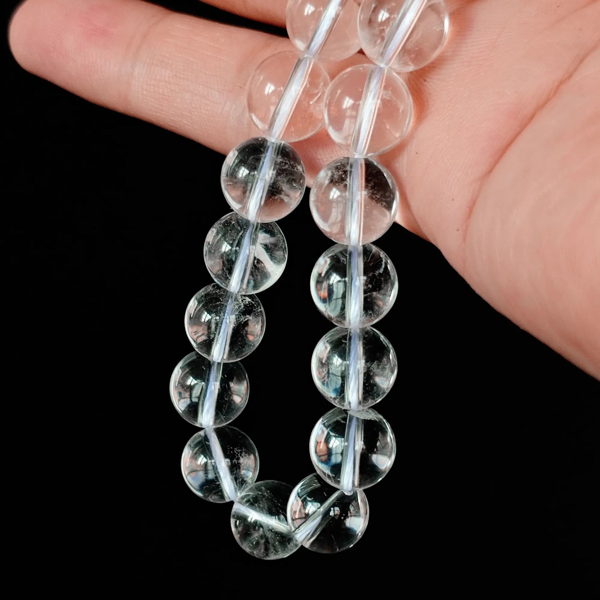 Close up of Grade A natural clear quartz round loose beads held between fingers, displaying high baseline transparency with subtle natural cotton inclusions