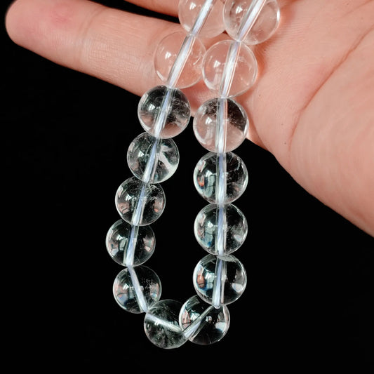 Close up of Grade A natural clear quartz round loose beads held between fingers, displaying high baseline transparency with subtle natural cotton inclusions